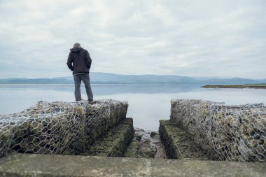Genç yakışıklı bir adam ayakta duruyor ve sakin deniz ve dağlarda hayatı düşünüyor. Etrafı beton deniz savunma duvarlarıyla çevrili. Ruh sağlığı ve depresyon iyileşme yolunda.