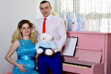 Çekici genç çift tatillerini evde kutluyor. Pembe bir piyanonun arka planında duruyor. Koca hamile karısına sarılıyor. Bir adam ve hamile karısı piyanonun başında duruyorlar. Ayakta ve