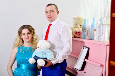 Çekici genç çift tatillerini evde kutluyor. Pembe bir piyanonun arka planında duruyor. Koca hamile karısına sarılıyor. Bir adam ve hamile karısı piyanonun başında duruyorlar. Ayakta ve