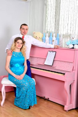 Çekici genç çift tatillerini evde kutluyor. Pembe bir piyanonun arka planında duruyor. Koca hamile karısına sarılıyor. Bir adam ve hamile karısı piyanonun başında duruyorlar. Ayakta ve