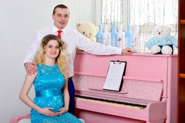 Çekici genç çift tatillerini evde kutluyor. Pembe bir piyanonun arka planında duruyor. Koca hamile karısına sarılıyor. Bir adam ve hamile karısı piyanonun başında duruyorlar. Ayakta ve