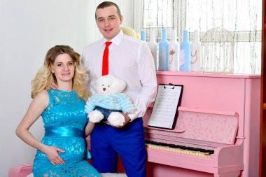 Çekici genç çift tatillerini evde kutluyor. Pembe bir piyanonun arka planında duruyor. Koca hamile karısına sarılıyor. Bir adam ve hamile karısı piyanonun başında duruyorlar. Ayakta ve