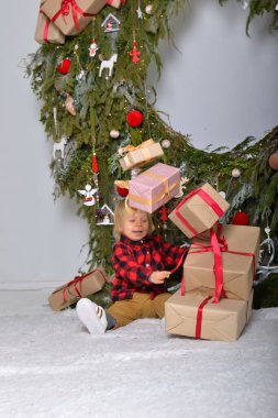 Mutlu çocuk yılbaşı çelenkleriyle süslenmiş Noel ağacının arka planında oturmuş Noel hediyeleriyle eğleniyor. Aile Noel konsepti.