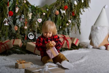 Mutlu çocuk yılbaşı çelenkleriyle süslenmiş Noel ağacının arka planında oturmuş Noel hediyeleriyle eğleniyor. Aile Noel konsepti.