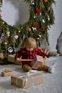 Mutlu çocuk yılbaşı çelenkleriyle süslenmiş Noel ağacının arka planında oturmuş Noel hediyeleriyle eğleniyor. Aile Noel konsepti.