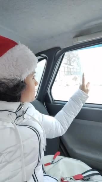 Девушка Шляпе Санта Клауса Сидит Машине Подмигивает Рисует Сердце Окне — стоковое видео
