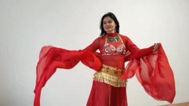 Kırmızı elbiseli bir dansçı beyaz arka planda doğulu bir dans ediyor. Profesyonel bir dansçı oryantal göbek dansı yapar. Kırmızı elbiseli seksi kadın beyaz bir stüdyoda baştan çıkarıcı bir dans yapıyor.