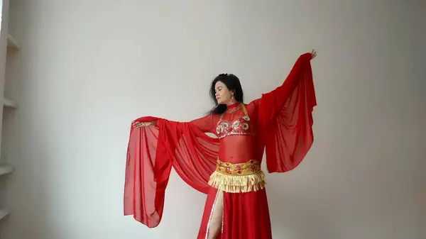 A dancer in a red suit is dancing with a red shawl an oriental dance on a white background. Free space for text. Banner. A professional dancer dances oriental belly dance. Sexy woman in red dress