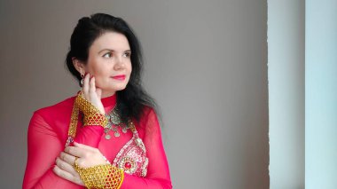 Kırmızı elbiseli bir dansçı beyaz arka planda doğulu bir dans ediyor. Metin için boş alan. Pankart. Profesyonel bir dansçı oryantal göbek dansı yapar. Kırmızı elbiseli seksi kadın baştan çıkarıcı danslar yapıyor.