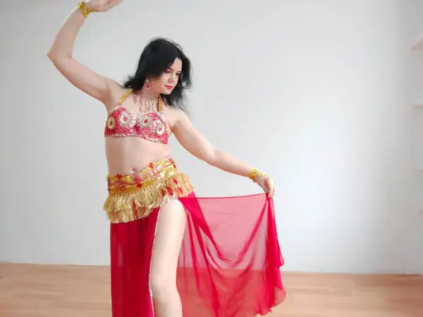 A dancer in a red suit is dancing an oriental dance on a white background. Free space for text. Banner. A professional dancer dances oriental belly dance. Sexy woman in red dress dances a seductive