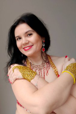 Kırmızı elbiseli bir dansçı beyaz arka planda doğulu bir dans ediyor. Profesyonel bir dansçı oryantal göbek dansı yapar. Kırmızı elbiseli seksi kadın beyaz bir stüdyoda baştan çıkarıcı bir dans yapıyor.