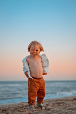 Denizin kenarında beyaz bir gömlek giyen mutlu çocuk deniz kenarına gidiyor. Mesaj için yer. Uzayı kopyala Kumsala giden mutlu çocuk dışarıda eğleniyor. Yaz tatili ve sağlıklı yaşam tarzı