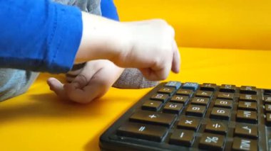 Okul ödevi sırasında hesap makinesiyle çocuk elleri. Çocuk parmaklarını tuşlara basar ve evde matematik çalışmayı hesaplar. Küçük bir çocuk sarı arka planda bir hesap makinesine güveniyor. Yüksek kalite 4K