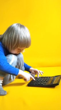 Küçük bir çocuk sarı arka planda bir hesap makinesine güveniyor. Çocuk parmaklarını tuşlara basar ve evde matematik çalışmayı hesaplar. Çocuk hesap makinesiyle aritmetik hesaplamalar yapıyor. Yüksek kalite 4K