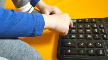 Okul ödevi sırasında hesap makinesiyle çocuk elleri. Çocuk parmaklarını tuşlara basar ve evde matematik çalışmayı hesaplar. Küçük bir çocuk sarı arka planda bir hesap makinesine güveniyor. Yüksek kalite 4K