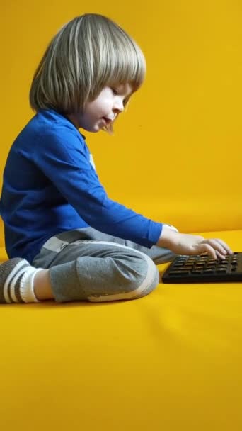 小さな子供は黄色の背景にある電卓で計算しています 子供の指のボタンを押して 自宅で数学を勉強することを計算します 子供は計算機を使って算術計算をする 高品質のフルHd — ストック動画