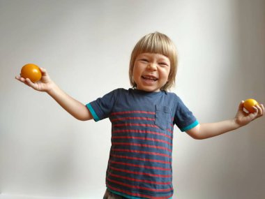 Küçük çocuk elinde domateslerle oynuyor ve gri arka planda onlarla eğleniyor. Çocuk ellerinde sebze ve domates tutuyor. Yüksek kalite fotoğraf