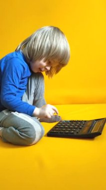 Küçük bir çocuk sarı arka planda bir hesap makinesine güveniyor. Çocuk parmaklarını tuşlara basar ve evde matematik çalışmayı hesaplar. Çocuk hesap makinesiyle aritmetik hesaplamalar yapıyor. Yüksek kalite 4K