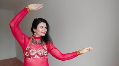 Kırmızı elbiseli bir dansçı beyaz arka planda doğulu bir dans ediyor. Şaşırtıcı duygular. Kız şaşırdı ve şoke oldu. Metin için boş alan. Pankart. Profesyonel dansçı.