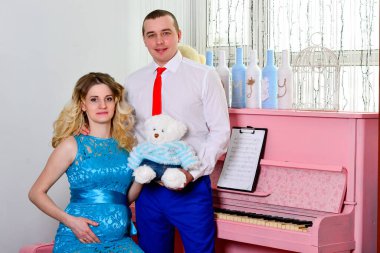 Çekici genç çift tatillerini evde kutluyor. Pembe bir piyanonun arka planında duruyor. Koca hamile karısına sarılıyor. Bir adam ve hamile karısı piyanonun başında duruyorlar. Ayakta ve