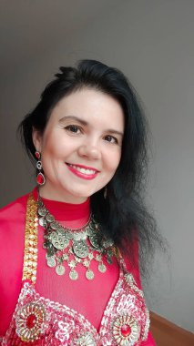 Kırmızı elbiseli bir dansçı beyaz arka planda doğulu bir dans ediyor. Profesyonel bir dansçı oryantal göbek dansı yapar. Kırmızı elbiseli seksi kadın beyaz bir stüdyoda baştan çıkarıcı bir dans yapıyor.