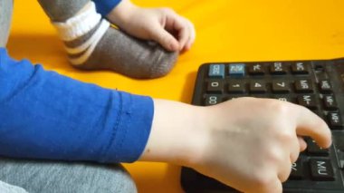 Okul ödevi sırasında hesap makinesiyle çocuk elleri. Çocuk parmaklarını tuşlara basar ve evde matematik çalışmayı hesaplar. Küçük bir çocuk sarı arka planda bir hesap makinesine güveniyor. Yüksek kalite