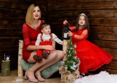 Küçük bir kız, bir oğlan ve anneleri Noel mumuna bakarlar. Ahşap arka plan. Yeni yıla ve Noel 'e hazırlanıyorum. Neşeli küçük bir kız, erkek ve kadın Noel fenerine bakar.