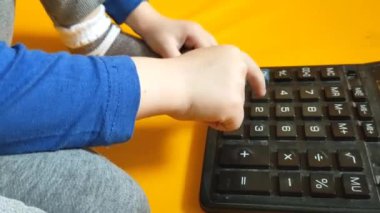 Okul ödevi sırasında hesap makinesiyle çocuk elleri. Çocuk parmaklarını tuşlara basar ve evde matematik çalışmayı hesaplar. Küçük bir çocuk sarı arka planda bir hesap makinesine güveniyor. Yüksek kalite