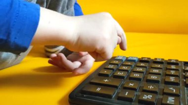 Okul ödevi sırasında hesap makinesiyle çocuk elleri. Çocuk parmaklarını tuşlara basar ve evde matematik çalışmayı hesaplar. Küçük bir çocuk sarı arka planda bir hesap makinesine güveniyor. Yüksek kalite 4K