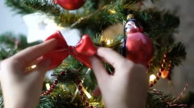 Kadınların ellerinin Noel ağacını toplarla süslemesi ve arka planda parlak festival ışıklarıyla kırmızı fiyonk yapması. Noel ağacı süslemek.