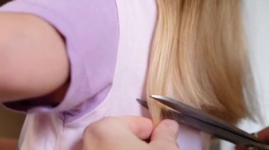 Hairdresser Trimming the Ends of a Blond Girls Hair. Mother doing daughters haircut at home.