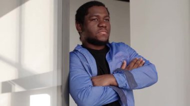 Profilde yakın plan siyah ciddi erkek yüzü var. Kolları bağlı bir adam ayakta duruyor. Ofiste pencereden dışarı bakan düşünceli Afrikalı Amerikalı bir adamın portresi karar verirken kameraya doğru dönüyor.. 