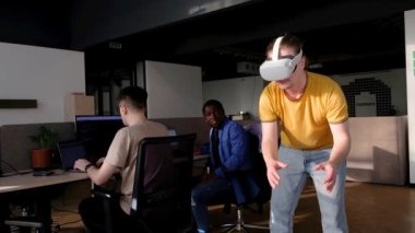 Bilgi İşlem Geliştirme Ekibi VR Projesi üzerinde çalışıyor. VR kulaklık takan, sanal dünyada bir şeylere dokunan ve çalan bir adam. Video oyunu yaratmak için VR teknolojileri ve bilgisayar kullanan çeşitli erkek programcılar 