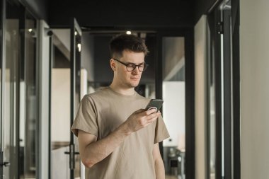 Ofis binasında, internet, geniş bant, 5G 'de cep telefonu kullanan ciddi bir genç. Ofisteki düşünceli adamın portresi..