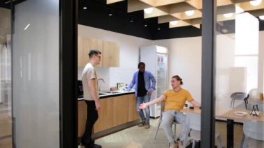 Group of cheerful young people talking and smiling during coffee break time in the office. Team of professional software developer relaxing in the canteen