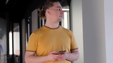 Ofis binasında, internet, geniş bant, 5G 'de cep telefonu kullanan ciddi bir genç. Ofisteki düşünceli adamın portresi..