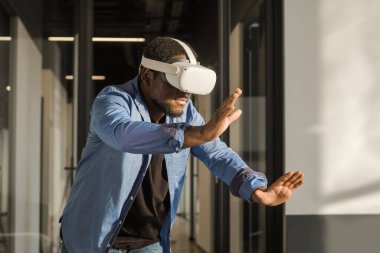VR kulaklıklı bir adam metaevren dünyasını keşfediyor, sanal gerçeklik deneklerine dokunuyor. Ofiste soyut siber dünya.