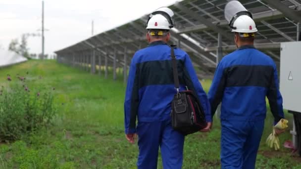 2人のサービスエンジニアまたは電気技師が変圧器の現場を確認し グリーンエネルギーの太陽光発電所の運転に関する問題を解決する 太陽光発電所の技術メンテナンス 太陽電池 — ストック動画