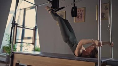 Atletik kadın, parlak bir spor salonunda Cadillac yenilikçi makinesinde ileri düzey pilates egzersizleri yapıyor..