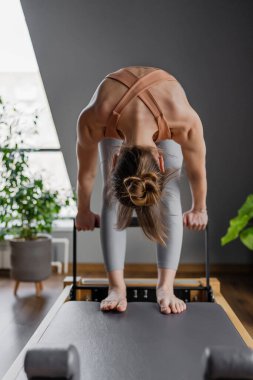 Jimnastik salonunda reformist bir makinede pilates yapan genç bir kadın. Fitness ve sağlık odaklı egzersiz.