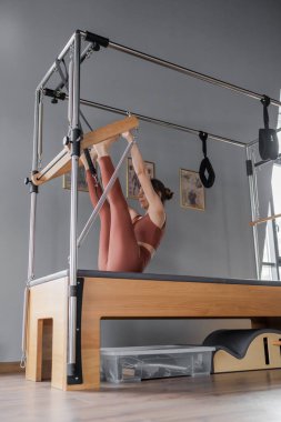 Modern bir fitness stüdyosunda, bir kadın dengeli bir Cadillac 'ta pilates antrenmanına enerjik bir şekilde katılıyor.