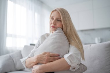 Yastık yastığına sarılan bir kadın modern bir evde stres, depresyon ve endişe gösteriyor.