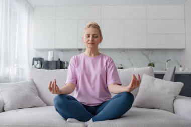 Son sınıf öğrencisi kadın bağdaş kurup yoga minderinde meditasyon yapıyor. Sakinlik ve rahatlığı kucaklıyor..