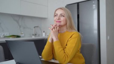 Sarışın bir kadın profesyonel dizüstü bilgisayar üzerinde çalışıyor ve doğal ışık alan rahat bir ofis ortamında notlar alıyor.