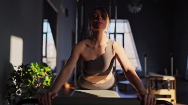 Aktif giyimli bir kadın güneşli bir stüdyoda göğüs ve sırt kasları için egzersiz yapıyor. Egzersiz yapmaya kendini adamış.