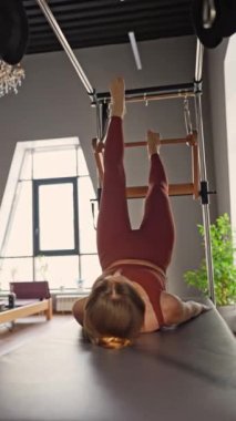 Modern bir fitness stüdyosunda, bir kadın dengeli bir Cadillac 'ta pilates antrenmanına enerjik bir şekilde katılıyor.