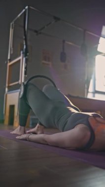 Bir kadın, stüdyoda Glute Köprüsü Pilates Antrenmanında kalça Sihirli Çember kullanıyor. Aktif olarak egzersiz yapıyor.