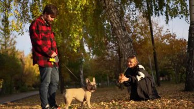 Bir adam parkta köpeğini gezdirirken, bir kadın sonbahar yaprakları ve ağaçlarla çevrili fotoğraf çekmek için diz çöker..