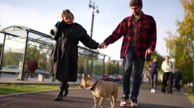 Renkli ağaçları ve açık gökyüzü olan güzel bir sonbahar parkında köpekleriyle yürüyüş yapan bir çift..