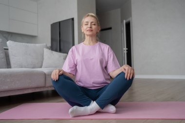 Son sınıf öğrencisi kadın bağdaş kurup yoga minderinde meditasyon yapıyor. Sakinlik ve rahatlığı kucaklıyor..